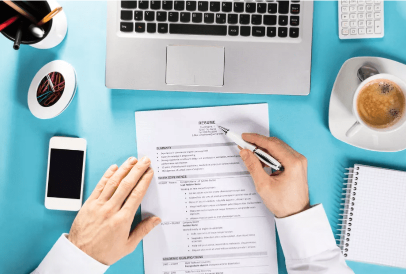 Key Components of a Winning Resume A professional reviewing a printed resume at a workspace with a laptop, smartphone, coffee cup, notepad, and office supplies on a blue desk.
