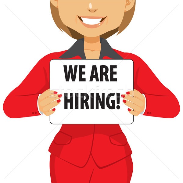 Smiling woman in red suit holding a "WE ARE HIRING!" sign
