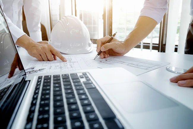 Engineers working on project blueprints near laptop